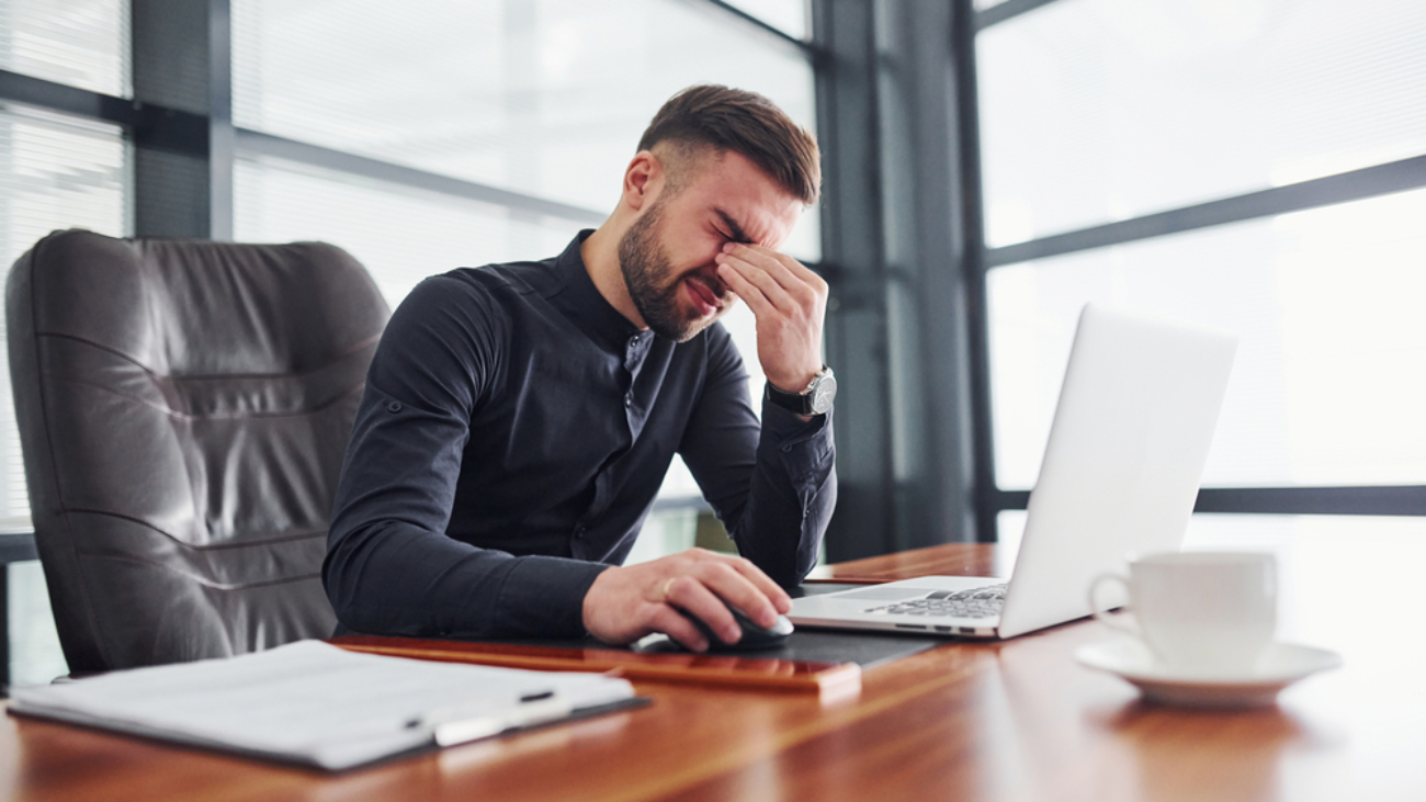 Man in formal clothes sitting by the table with laptop and feels bad.