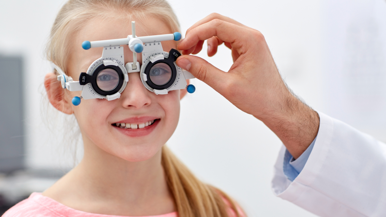 health care, medicine, people, eyesight and technology concept - optometrist with trial frame checking girl patient vision at eye clinic or optics store