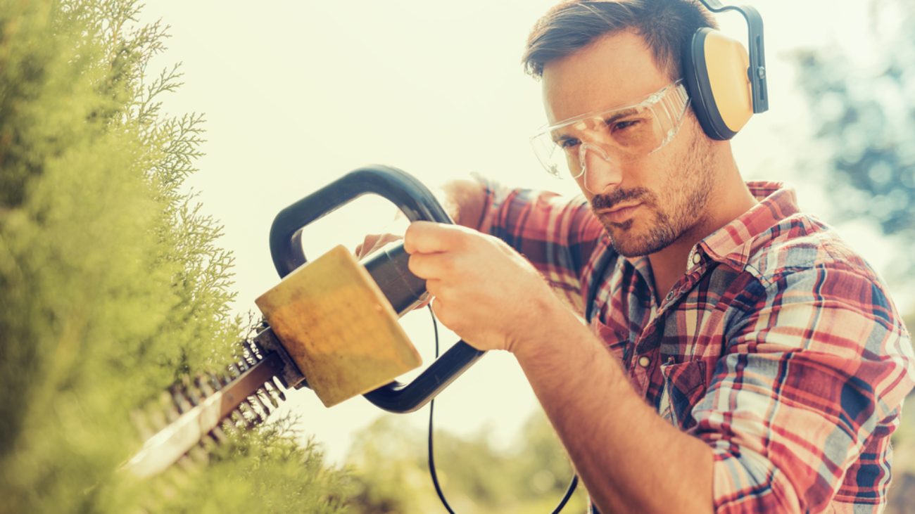 Man cutting a hedge with electrical hedge trimmer - eye injury prevention month