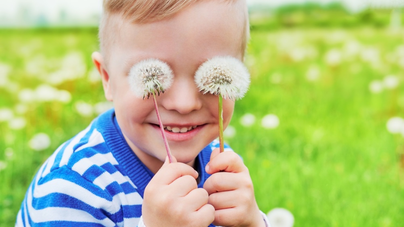 Happy face kid smile.Close up portrait joy child outdoors. Little boy playful smiling holding dandelions on eyes as eyeglasses. Joyful childhood, summer day. Background green grass