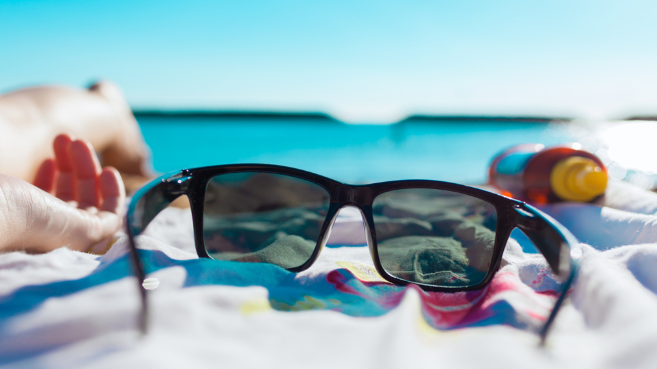 dark summer sunglasses on bright summer day on beach towel with blue water in the background