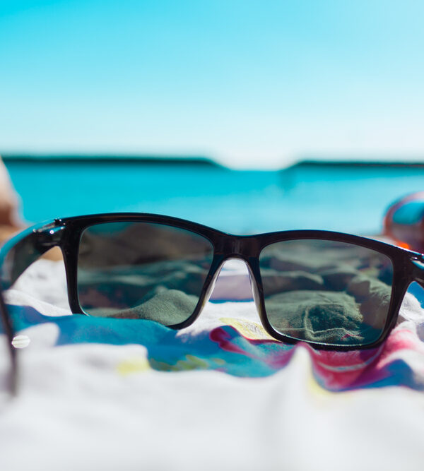 dark summer sunglasses on bright summer day on beach towel with blue water in the background