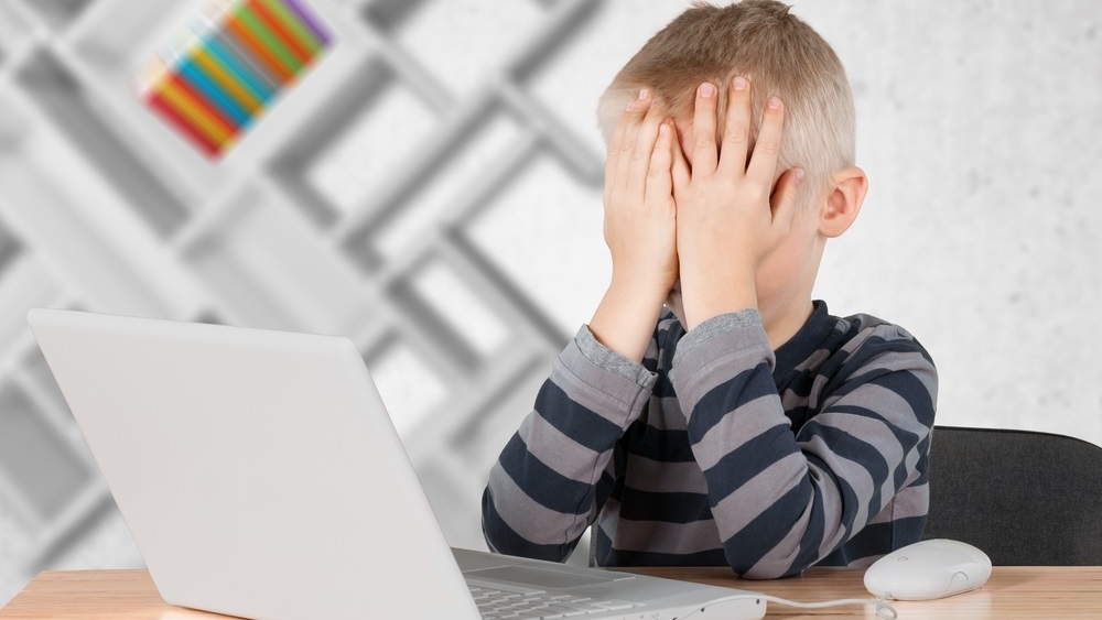 A Little Boy With His Hands Over His Eyes Sitting In Front Of His Computer