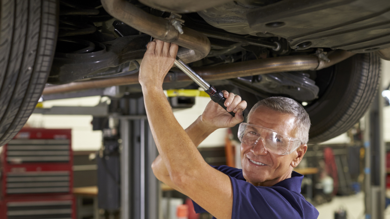 man working on underside of car wearing safety glasses