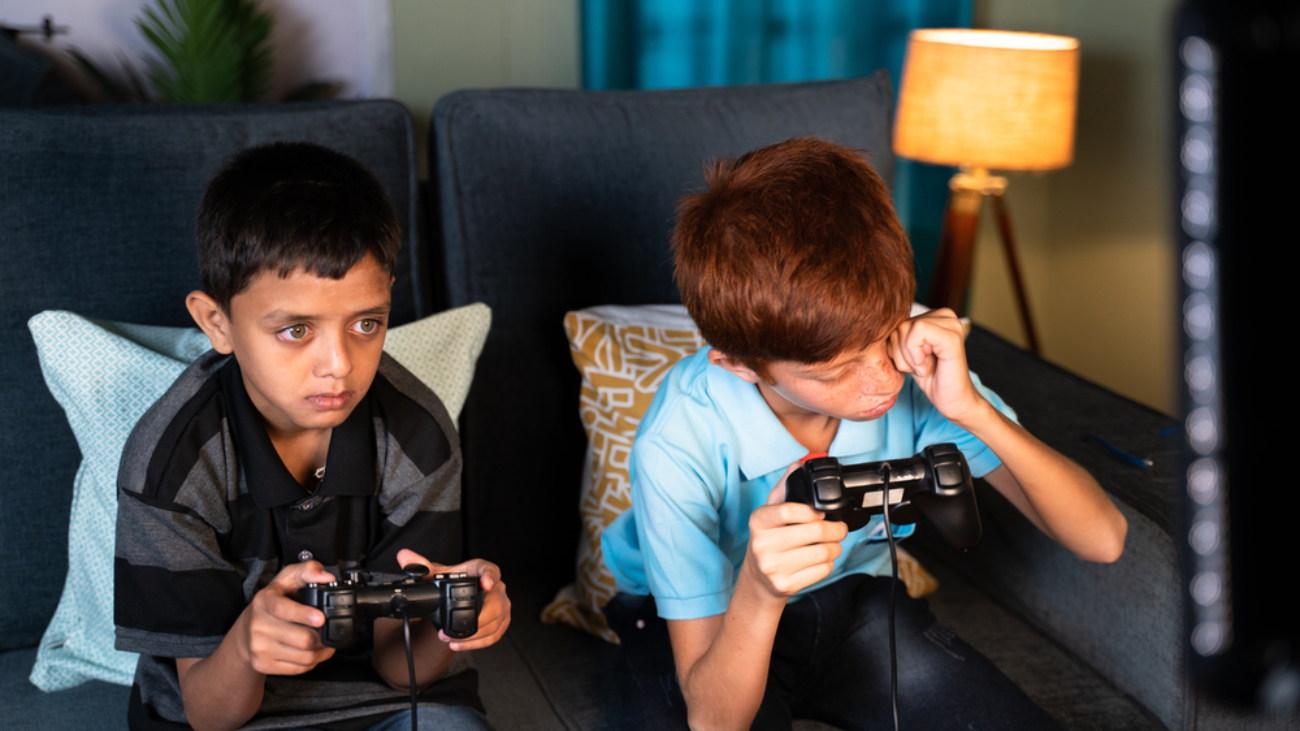 Parent Tips to Manage Eye Strain: concept of eye strain due to over night video game play - Two kids playing video game during late night at home and one kid rubbing his eyes due eye irritations.