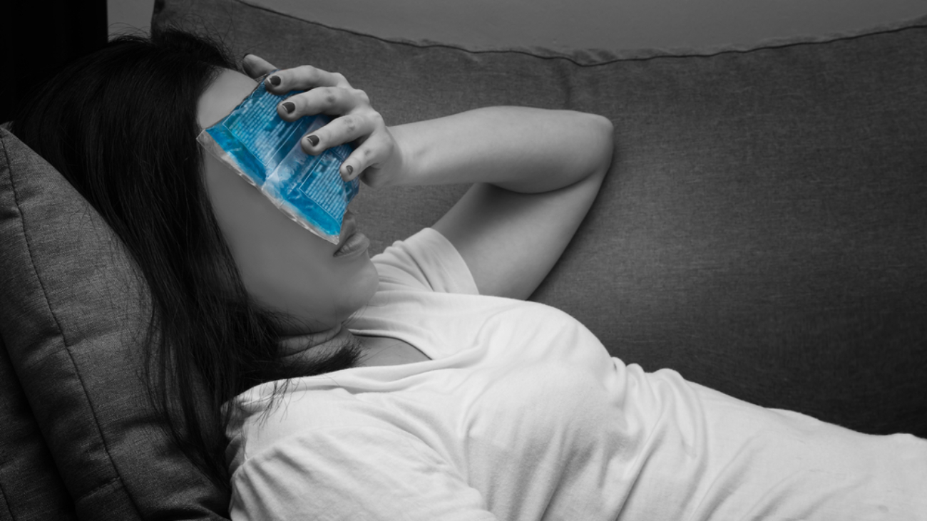 young woman lying on couch with coldpack over her eyes with migraines