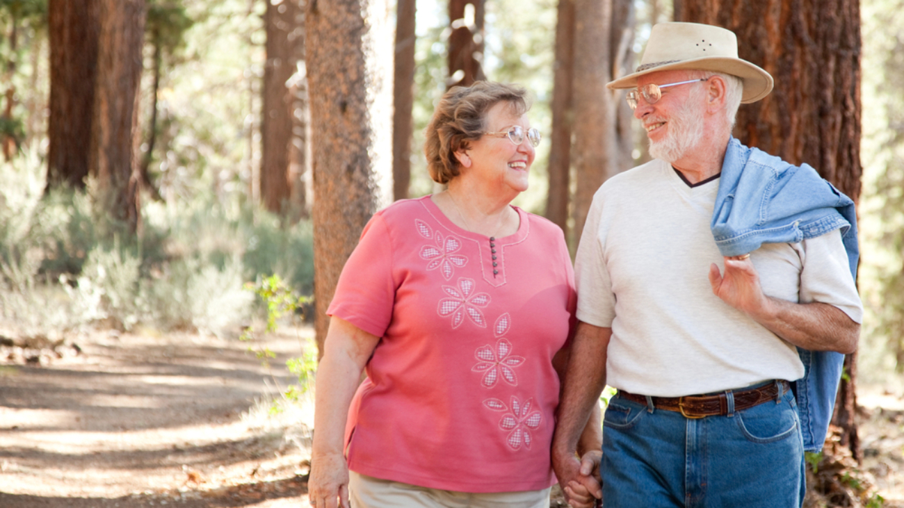 Senior couple walking hand in hand, gleaming at each other with eye glasses on, in the outdoors with big trees in the backgroundWays to Prevent Vision Loss