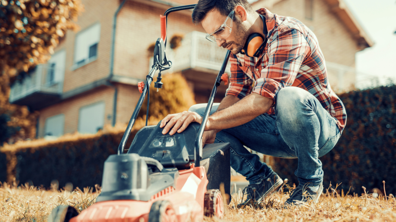 Man in plaid shirt working on lawn mower in garage, representing eye injury prevention safety around the home