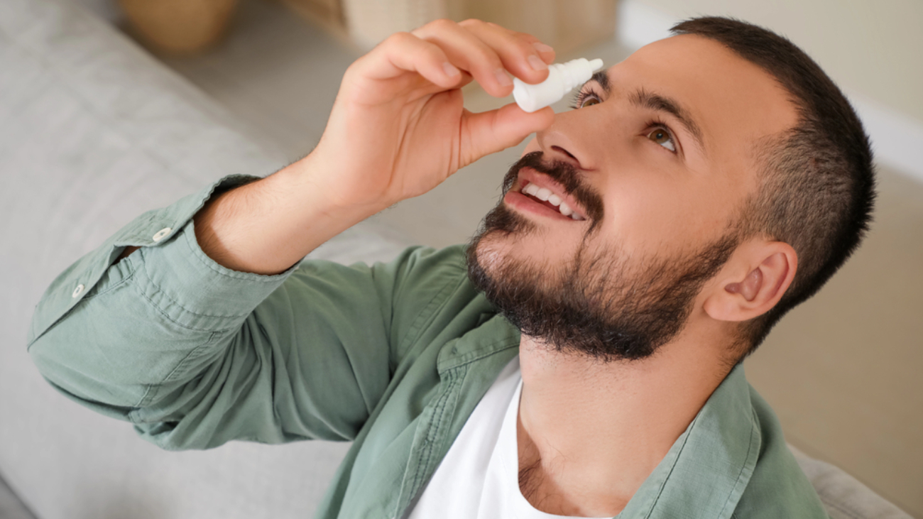 man wtih head tilted back putting eye drops in eyes pink eyes
