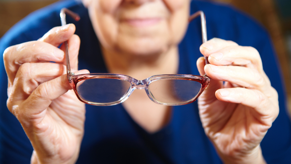 senior individual in blue shirt preparing to put on a pair of e-scoop eyewear glasses