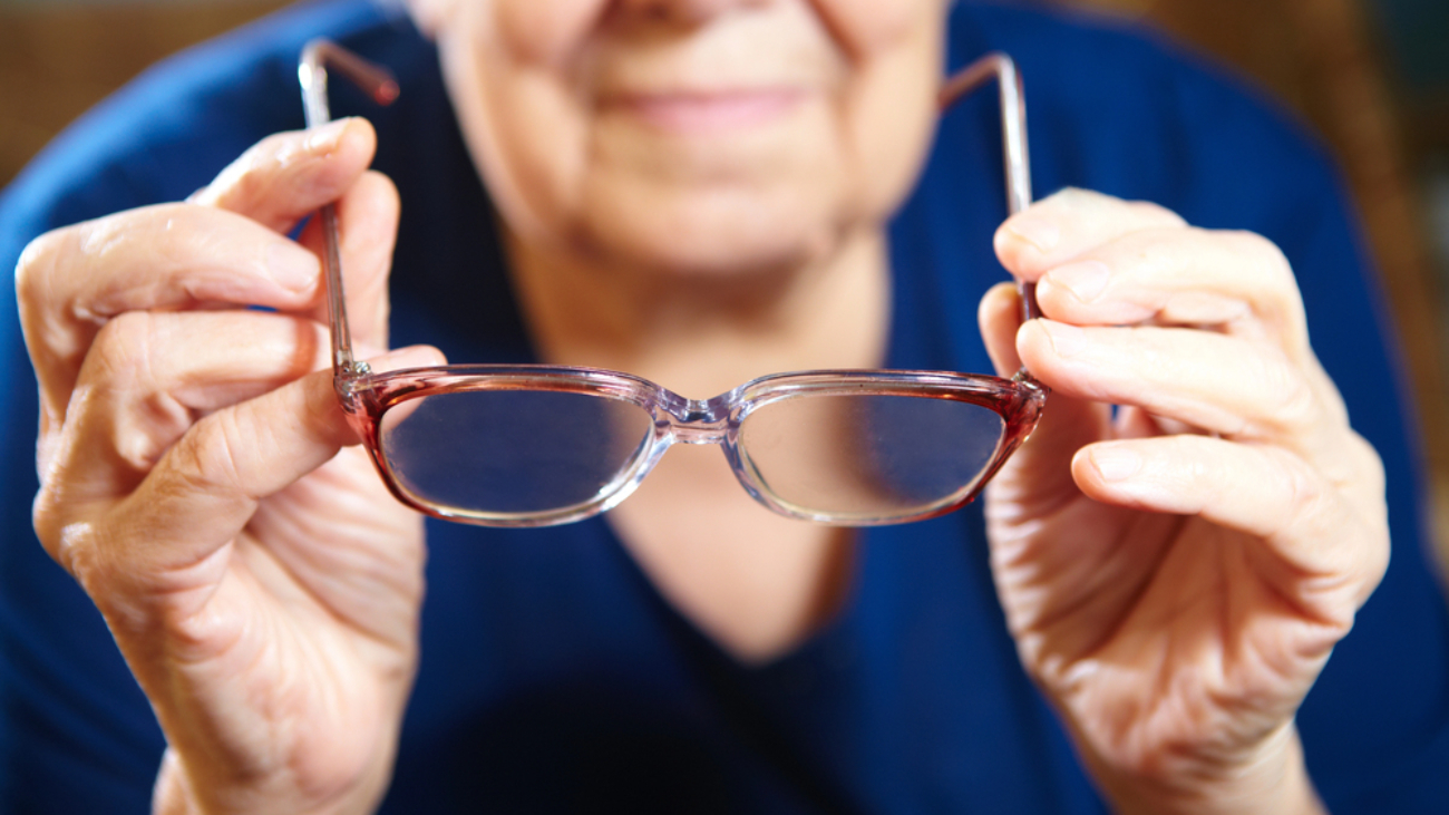 senior individual in blue shirt preparing to put on a pair of e-scoop eyewear glasses
