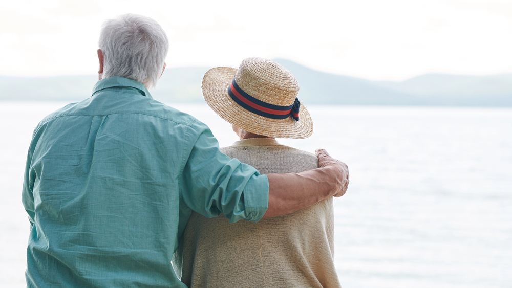 senior couple sitting arm in arm in front of a body of water representing summer with low vision