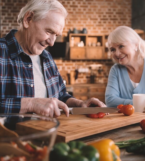 senior man and woman in kitchen cutting fresh tomatoes