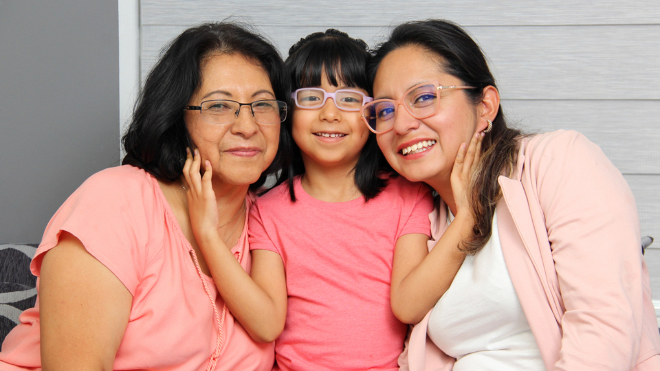 Two smiling woman wearing glasses with a young child between them also smiling and wearing glasses