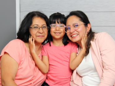 Two smiling woman wearing glasses with a young child between them also smiling and wearing glasses