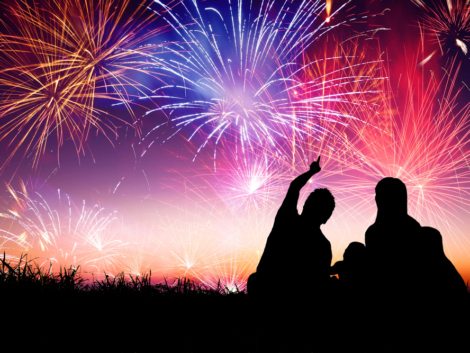 silhouette image of a family sitting in the grass pointing to the sky with fireworks